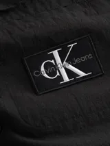 Camisa negra de manga larga Calvin Klein Jeans confeccionada en tejido texturizado de algodón. Presenta cuello camisero, cierre con botones, bolsillo en el pecho con insignia del logo de la marca y puños con botones.