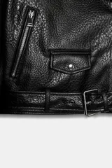 Cazadora tipo biker de corte corto y diseño holgado con hombreras. Presenta cuello con solapas, cierre frontal cruzado con cremallera, bolsillos laterales con cremallera y un bolsillo pequeño con solapa y botón a presión. Incluye un cinturón ajustable en el bajo y cremalleras en los puños.