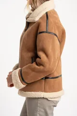Campera tipo gamulán de corte oversize, confeccionada en material efecto gamuza color camel con interior y detalles de cuello y puños en corderito sintético color crema. Presenta cierre frontal y detalles de ribetes en cuero sintético negro.