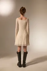 Vestido corto de encaje color crema, con mangas largas, cuello en V y falda evasé con terminación de volado.