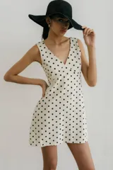 Vestido corto color crema con estampado de lunares negros, escote en V y sin mangas.