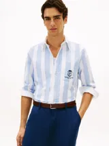 Camisa de corte clásico de puro algodón Oxford, con diseño de rayas verticales en color celeste y blanco. Cuenta con cuello abotonado, bolsillo frontal de parche con un escudo bordado y mangas largas con puños redondeados.
