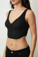 Top negro ajustado al cuerpo con escote en V profundo y tirantes anchos. Presenta un tejido texturizado, posiblemente encaje o jacquard, con un corte estilo corsé en la parte inferior.