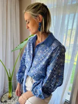 Camisa de manga larga con diseño de flores bordadas en color blanco sobre base azul. Presenta cuello clásico, cierre frontal con botones y mangas abullonadas con puños elásticos.