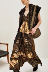 Vestido largo de corte fluido con estampado estilo batik en tonos oscuros, marrones y crema. Presenta un diseño inspirado en pañuelos con volado en el ruedo y escote en V.