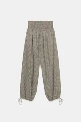 Pantalón de tiro medio con estampado de cuadros vichy en tonos beige y marrón. Cuenta con cintura elástica tipo nido de abeja y bajo ajustable con cordones.