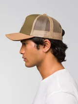 Gorro trucker de color verde militar, con visera curvada marrón claro, panel frontal rígido y red trasera. Cuenta con un parche circular bordado en la parte delantera y cierre ajustable snapback.