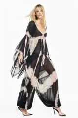 Bata de chiffon negro con mangas largas acampanadas, detalles de encaje beige en los bordes y lazos frontales. Presenta un diseño fluido y semitransparente.