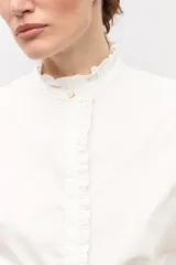 Camisa blanca de manga corta con cuello mao y detalles de volados a lo largo de la botonera frontal y en los puños.