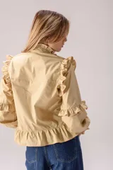 Camisa celeste con volados decorativos en los hombros, pecho, mangas y ruedo, destacados con ribetes en tono rojo. Presenta cierre frontal de botones, cuello alto y mangas largas abullonadas con puños ajustados.