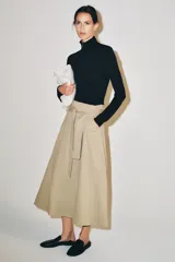 Falda midi color beige confeccionada en hilatura con mezcla de algodón. Presenta tiro medio, cintura con trabillas, bolsillos laterales ocultos en costura y cinturón del mismo tejido. Su diseño incluye un bajo acabado en línea evasé y cierre lateral con cremallera.