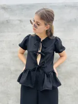 Blusa estampada con hojas verdes y blancas, con escote en V y mangas cortas abullonadas. Presenta volados en el ruedo y detalle de lazos en el frente.