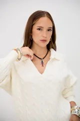 Sweater de punto grueso color crudo, con cuello polo y escote en V. Presenta un diseño de trenzas en toda la prenda y es de corte holgado.