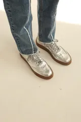 Zapatilla de estilo urbano en color plateado metalizado, con cordones al tono y suela de goma color marrón.