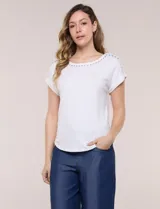 Remera blanca de punto acanalado con escote redondo adornado con tachas metálicas en el cuello y hombros, mangas cortas japonesas y ruedo curvo.