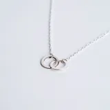 Collar de cadena fina con dije de dos argollas entrelazadas de diseño minimalista, confeccionado en plata 925.