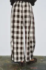 Pantalón de tiro medio con cintura elástica, pierna ancha y bolsillos laterales ocultos. Presenta un estampado de cuadros vichy en blanco y negro/marrón oscuro.