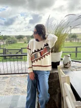 Sweater de punto color crema con diseño geométrico en tonos marrones, naranjas, verdes y grises en el pecho y las mangas. Confeccionado con lana y cuero, con detalles tejidos y bordados a mano.