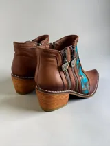 Botas cortas de cuero marrón terracota con diseño pintado a mano en la parte frontal en tonos turquesa y dorado. Cuentan con taco cuadrado de madera, doble cierre lateral con tiradores metálicos personalizados y punta fina.