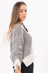 Buzo tejido de punto bicolor en tonos crudo y gris, con silueta relajada, mangas amplias con jaretas regulables en los puños y cuello redondo.