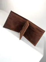 Billetera masculina confeccionada en cuero, con diseño bicolor en tonos marrón claro y oscuro. Presenta un detalle grabado de un búho en la parte frontal.