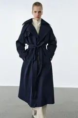 Trench oversize de Zara Woman Collection, color azul marino, confeccionado en hilatura con mezcla de algodón. Presenta cuello solapa, manga larga ajustable con trabillas, bolsillos delanteros y cinturón del mismo tejido con lazadas. Destacan los pespuntes marcados a tono y el cierre frontal cruzado con botones.