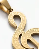 Dije con forma de clave de sol, elaborado en acero con baño dorado, con textura punteada en su superficie.