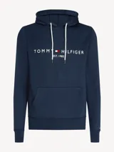 Hoodie azul marino de Tommy Hilfiger con capucha ajustable mediante cordones blancos. Presenta un bolsillo tipo canguro en la parte frontal y el logo de la marca bordado en el pecho junto a la inscripción 'EST. 1985'.