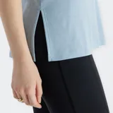 Musculosa deportiva New Balance Sport Essentials, color celeste claro, con cuello redondo y logo NB plateado en el pecho. Presenta un corte holgado y aberturas laterales.