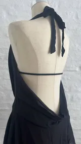 Vestido corto negro con escote halter y cuello drapeado. Presenta un diseño ajustado en la parte superior y falda con volados en la parte inferior.