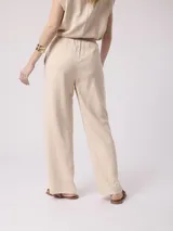 Pantalón fluido de color beige, con cintura elástica con cordón de ajuste y costuras frontales a lo largo de las piernas.