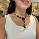 Collar corbatero de bronce con piedras naturales engarzadas. El diseño central presenta una piedra turquesa ovalada, flanqueada por piedras rojas y piedras ojo de tigre ovaladas. De esta piedra central cuelga una cascada de piedras rojas y ojo de tigre engarzadas en marcos de bronce.