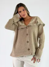 Saco de punto calado color beige, con cuello grande y volados con bordados florales blancos, cierre frontal con botones y mangas largas con puños anchos.