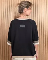 Buzo de punto negro con diseño holgado, mangas codo y detalles en tono tostado y blanco en el cuello redondo, puños y ruedo.