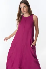 Vestido sin mangas, color fucsia intenso, de corte amplio y largo midi. Presenta un corte central vertical y bolsillos laterales.