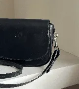 Cartera bandolera de cuero natural color marrón, con estructura rígida, costuras a la vista y logo grabado en el frente.