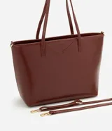Cartera tipo shopper grande de Satinato, confeccionada en poliuretano con textura efecto crocco en color marrón. Presenta doble asa fija, correa larga desmontable con herrajes dorados y cierre superior por cremallera.
