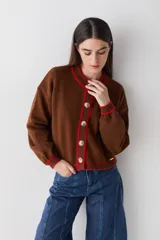 Cardigan de punto color marrón con detalles de ribete en color verde oliva en cuello, puños, ruedo y tapeta de botones. Presenta cierre frontal con botones grandes y un pequeño bordado en el pecho.