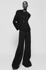 Pantalón de tiro alto con diseño flare, confeccionado en tela de color negro. Presenta cinco bolsillos, cintura con trabillas y cierre frontal con cremallera y botón.