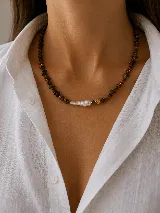 Collar de piedras naturales en tonos marrones, con un dije central de perla barroca alargada y un pequeño cubo dorado decorativo.