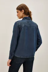 Camisa de denim azul oscuro con cuello clásico, cierre frontal de botones y mangas largas. Presenta un delicado bordado de motivos florales y vegetales realizado con cuentas y canutillos en tono azul marino.