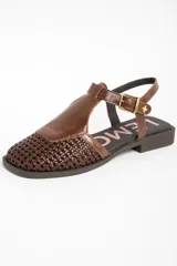 Sandalias de cuero marrón, con puntera cerrada de diseño trenzado, empeine liso y tira ajustable con hebilla en el talón. Cuenta con suela plana y baja.
