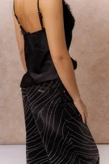 Pantalón wide leg de tiro alto en denim negro, con diseño de líneas onduladas formadas por pequeñas aplicaciones de brillos. Cuenta con cierre frontal, bolsillos funcionales y pasacintos.