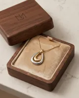 Collar de acero con baño de oro, compuesto por una cadena fina y un dije colgante en forma de lágrima con diseño bicolor en tonos dorado y plateado.