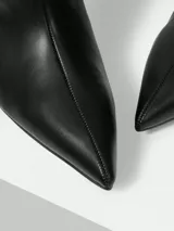 Bota de caña alta en color negro, confeccionada en cuero con acabado suave. Presenta un diseño de punta fina y un tacón tipo kitten heel, ofreciendo una silueta elegante y sofisticada.
