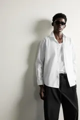 Camisa de vestir blanca de corte slim fit, confeccionada en tejido de algodón con textura estructurada. Cuenta con cuello italiano, mangas largas con puños abotonados y cierre frontal con botonadura.