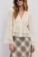 Blusa marfil con detalles de encaje y bordados florales transparentes, con escote en V, cierre frontal abotonado y mangas largas acampanadas.