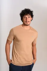 Remera de manga corta con cuello redondo, confeccionada en algodón de color beige. Presenta un pequeño logo bordado de un pingüino en el pecho.