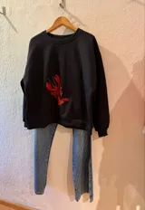 Buzo negro de corte holgado con estampa de una langosta roja en el frente.