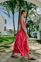 Vestido largo sin mangas con escote en pico y tirantes anchos. Presenta un diseño de rayas verticales en tonos fucsia y rojo, con detalle de falsos botones frontales y cierre de cremallera oculto en la espalda.